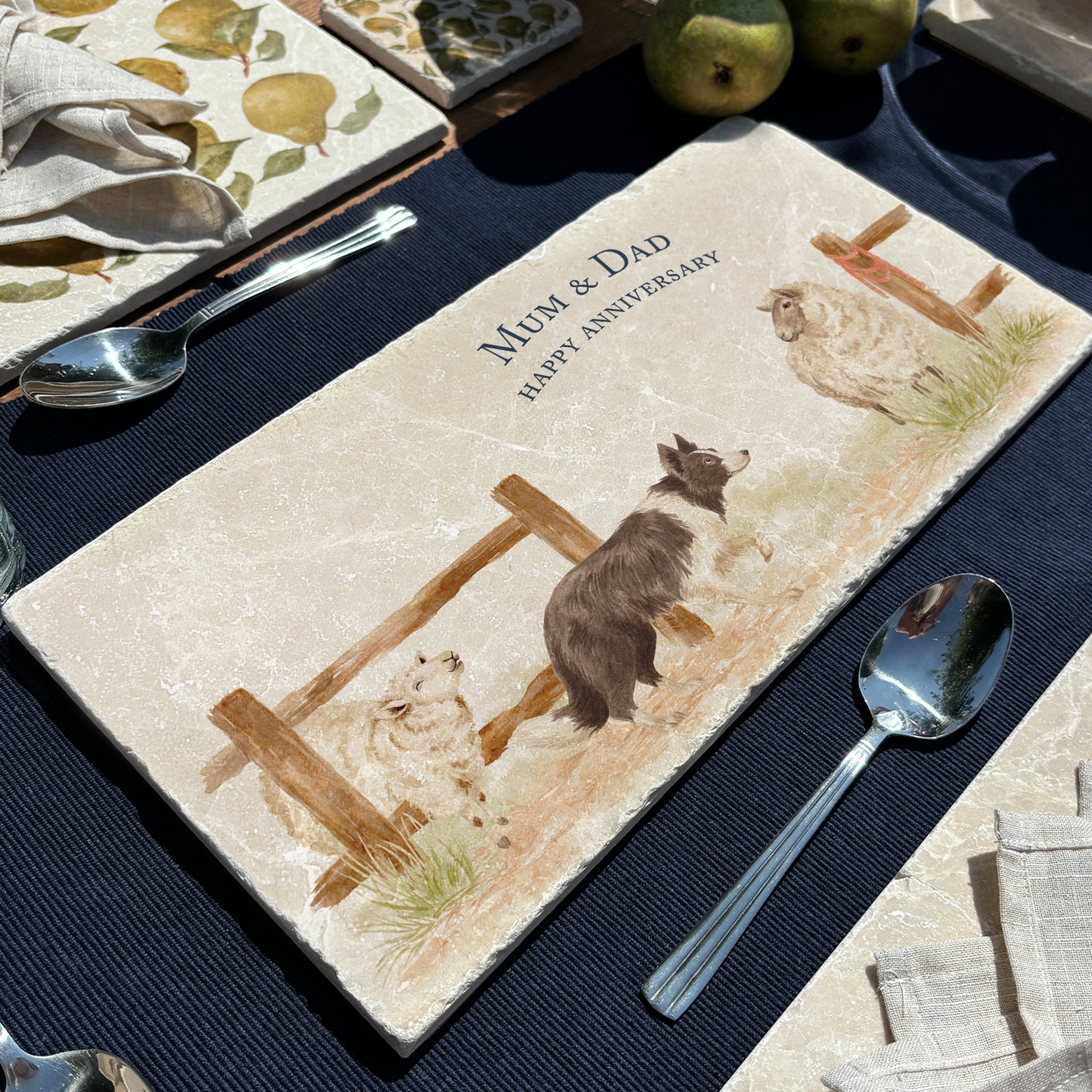 A rectangular marble sharing platter with a watercolour design of a border collie working dog herding sheep through a gate on the farm. The platter is personalised with custom text and set on a wooden country kitchen table.