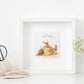 A framed greetings card with a watercolour design of rabbits in flowerpots eating flowers. The Card reads 'Just For You'.