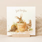 A square greetings card with a watercolour design of rabbits in flowerpots eating flowers. The Card reads 'Just For You'.