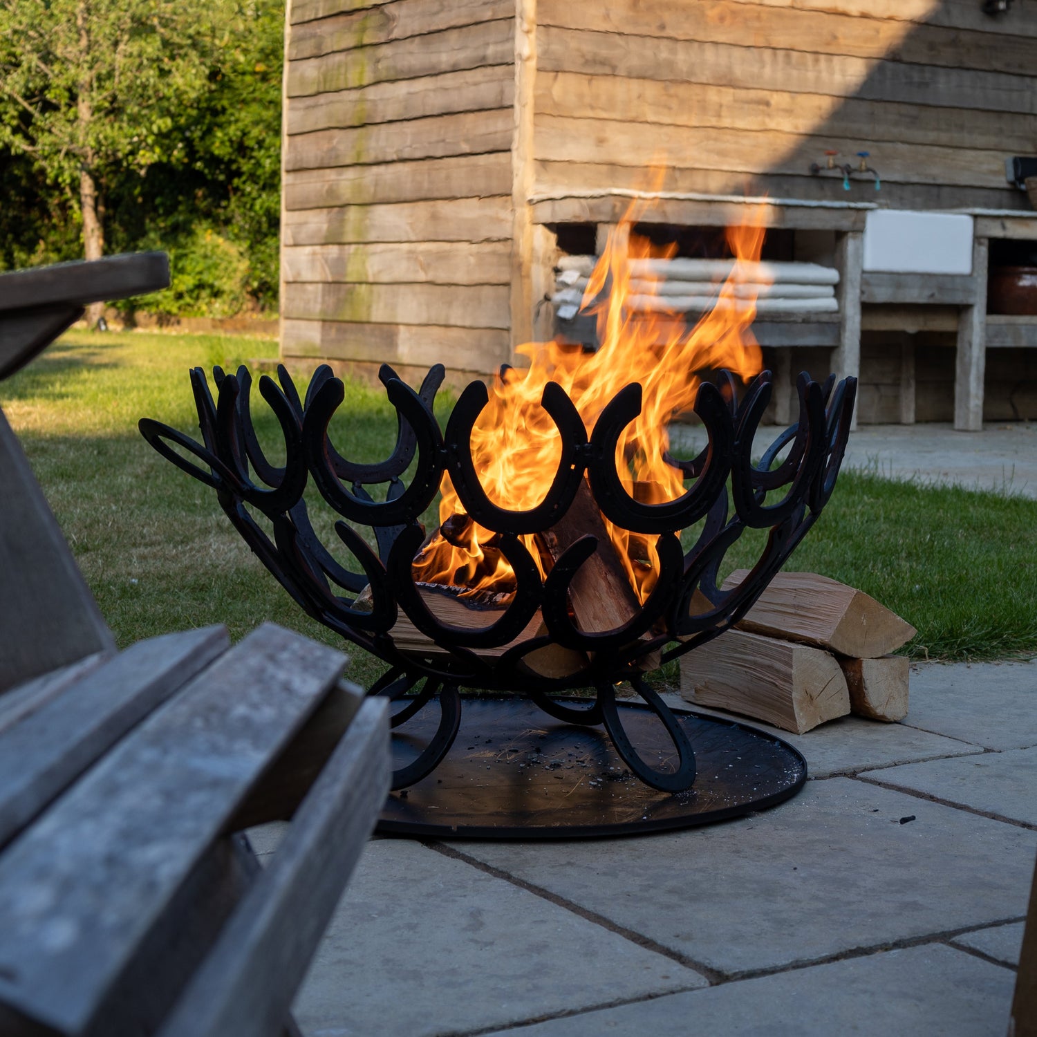 Outdoor fire pit made from horseshoes with flames in front of a wooden cabin