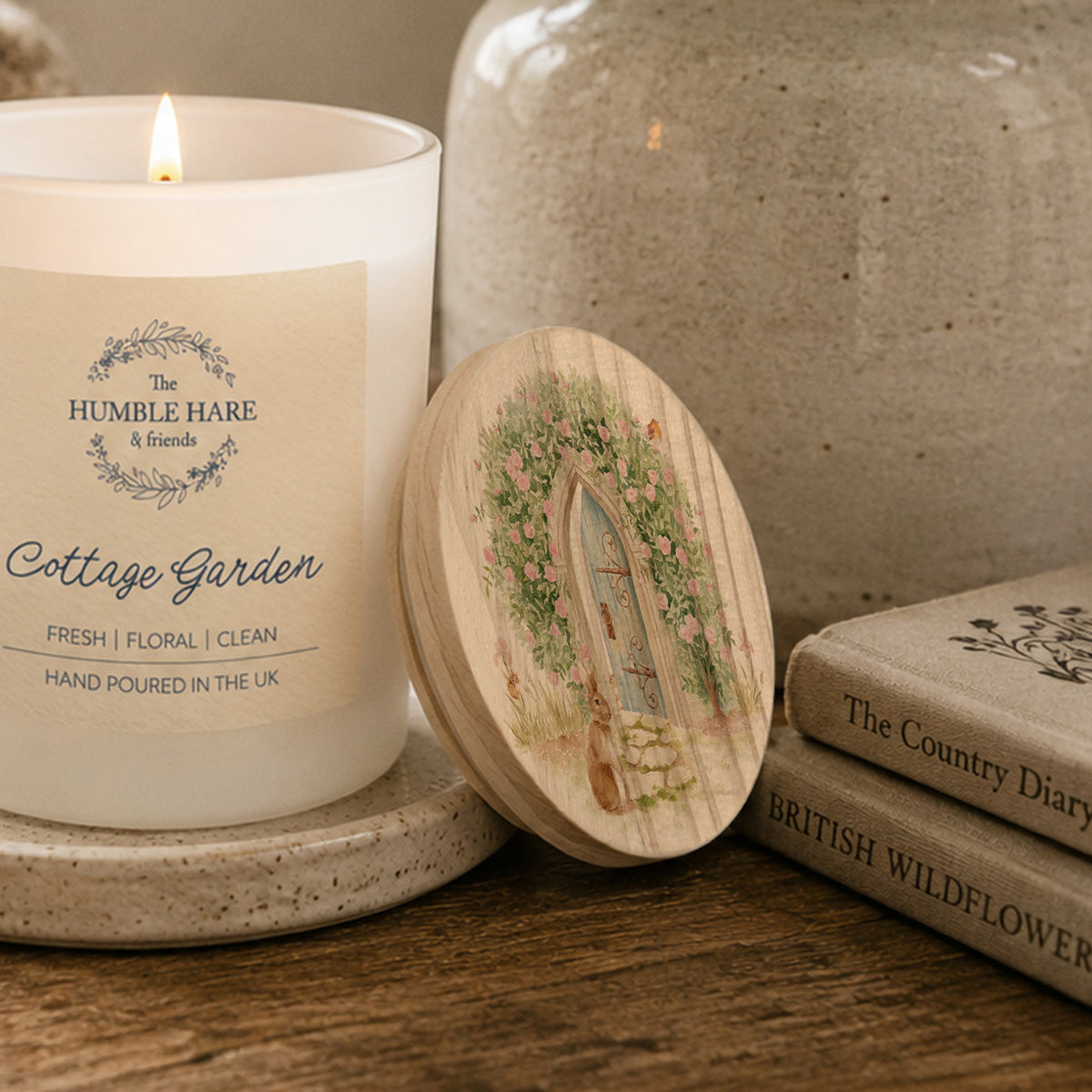 A wooden candle lid with a watercolour illustration of a hidden garden.