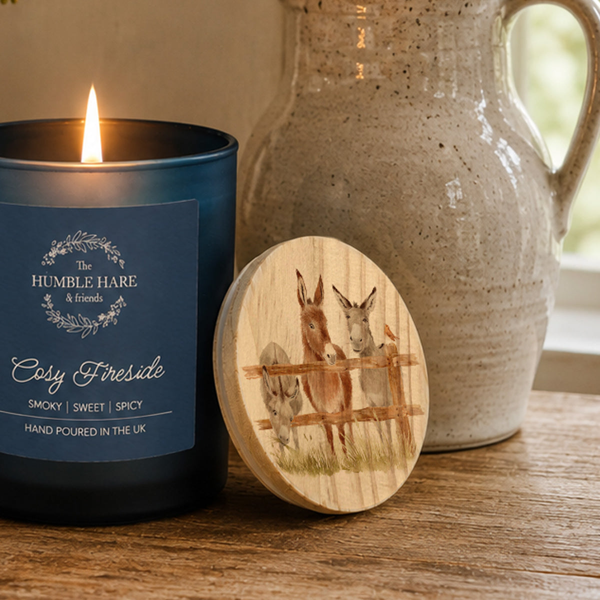 A wooden candle lid with a watercolour illustration of donkeys.
