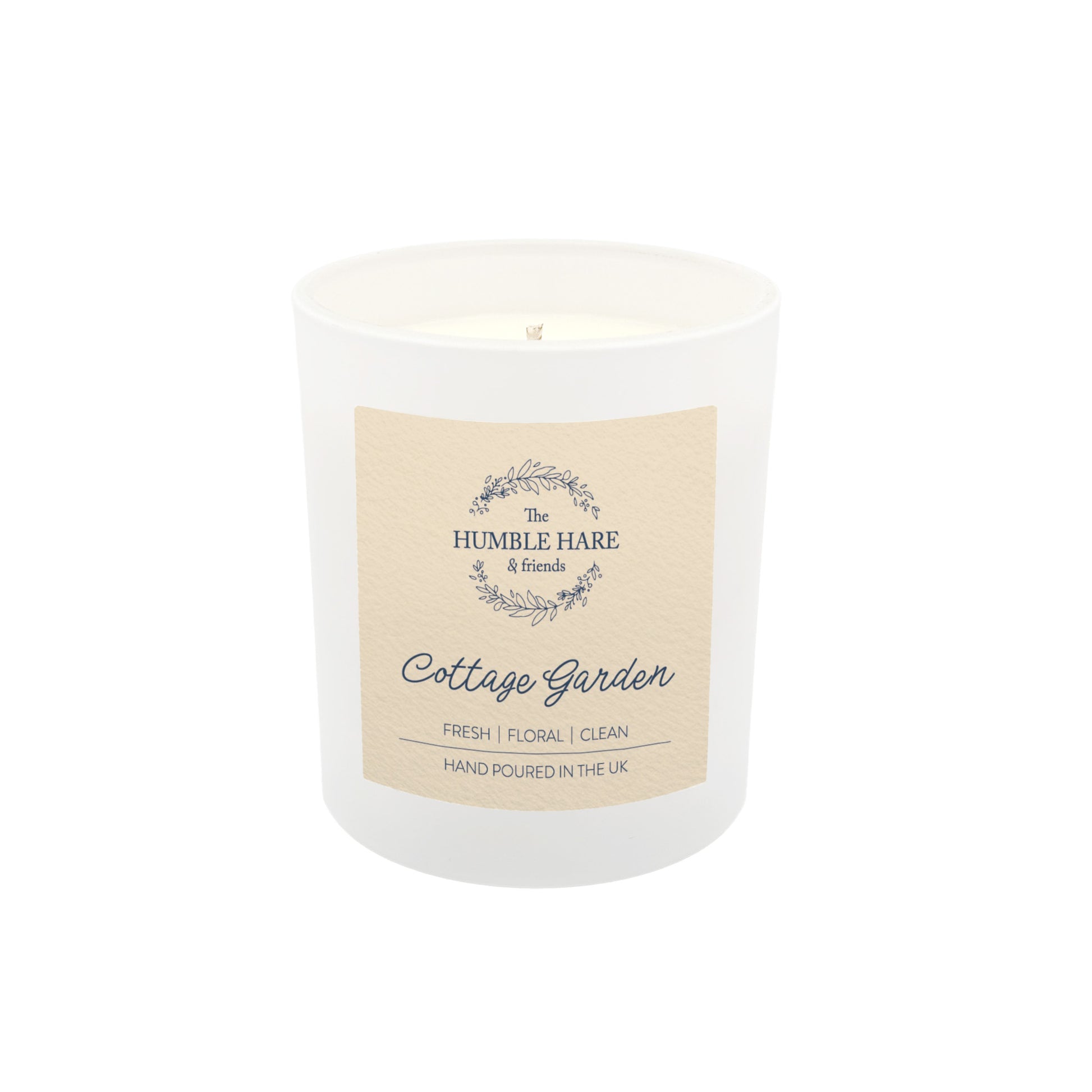 A white glass jar soy wax candle with a cream paper label. The candle is The Humble Hare's Cottage Garden, a floral clean washing scent.