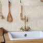 A rustic country kitchen sink and brass tap in front of a cream marble tiled splashback, made up of 20x40cm natural marble tiles.