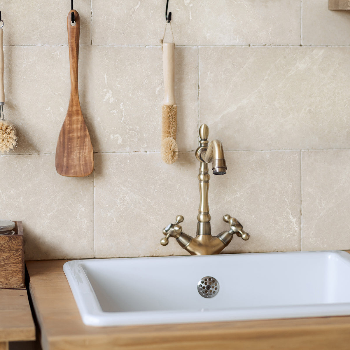 A rustic country kitchen sink and brass tap in front of a cream marble tiled splashback, made up of 20x40cm natural marble tiles.