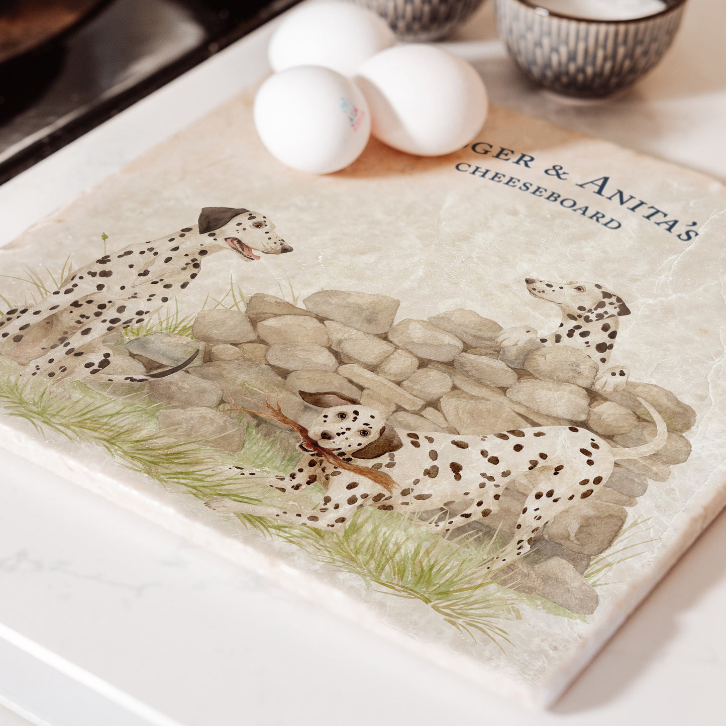 A large square marble platter featuring a  watercolour design of 3 dalmatian dogs and personalised with custom text. The platter is sat next to an aga in the kitchen.