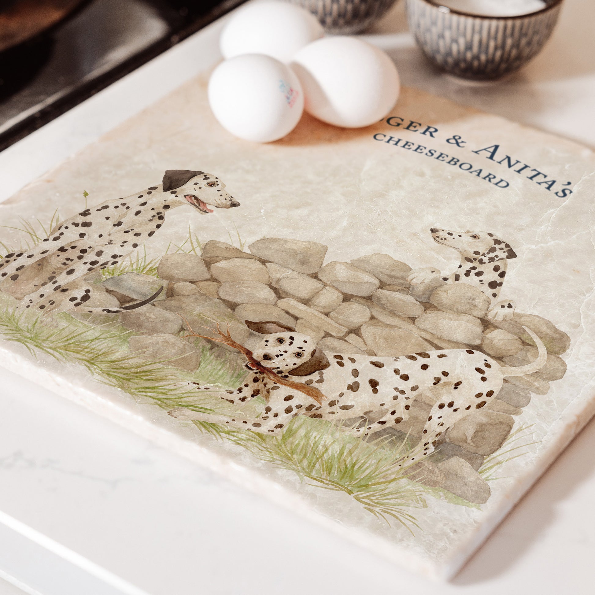 A large square marble platter featuring a  watercolour design of 3 dalmatian dogs and personalised with custom text. The platter is sat next to an aga in the kitchen.