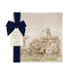 A square marble platter featuring a  watercolour design of 3 dalmatian dogs playing in the countryside. The platter is propped up against a kitchen counter. The platter is packaged with a luxurious blue gift bow.