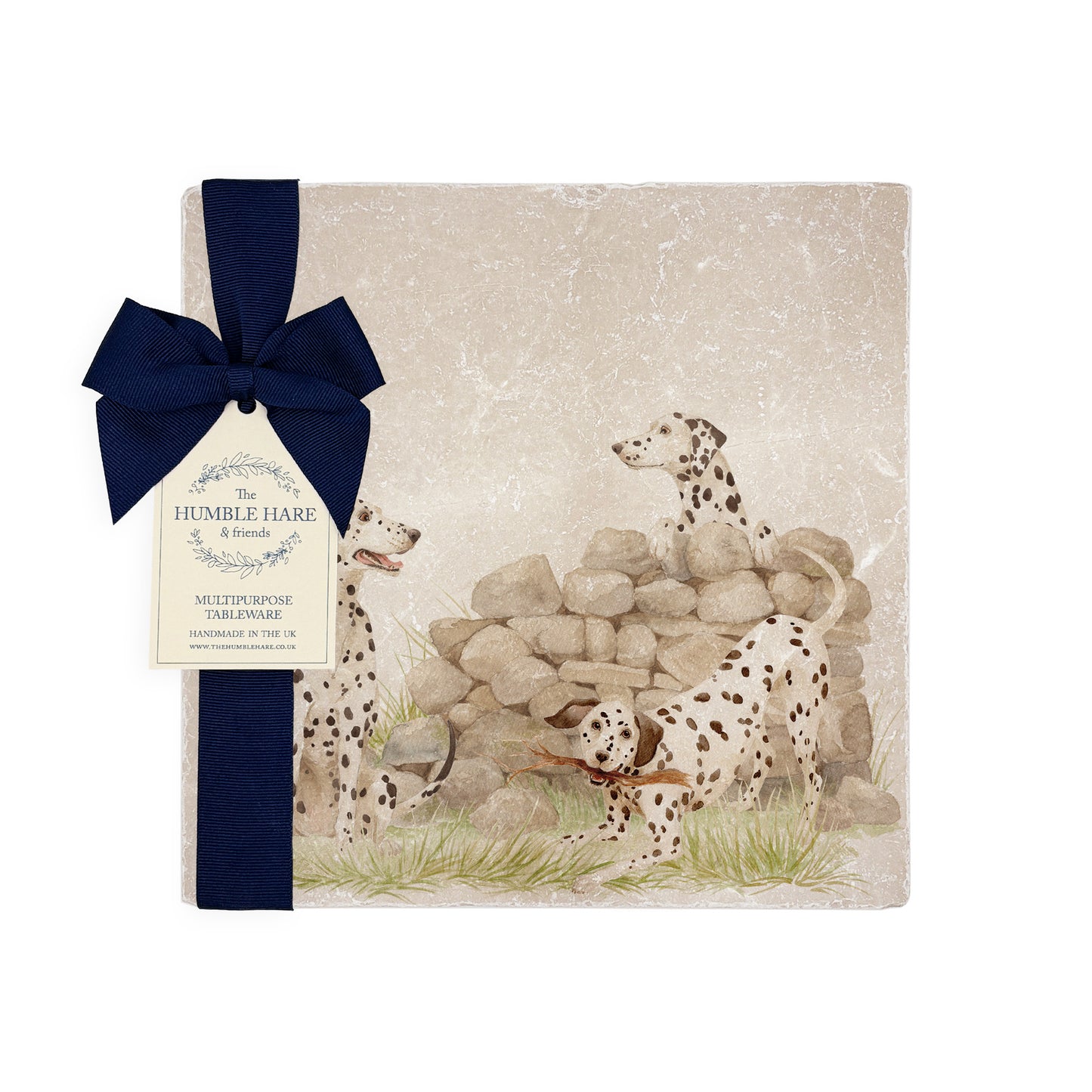 A square marble platter featuring a  watercolour design of 3 dalmatian dogs playing in the countryside. The platter is propped up against a kitchen counter. The platter is packaged with a luxurious blue gift bow.