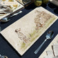 A rectangular marble sharing platter featuring a watercolour design of 3 dalmatian dogs playing fetch in the countryside. The platter is set on a dining table.
