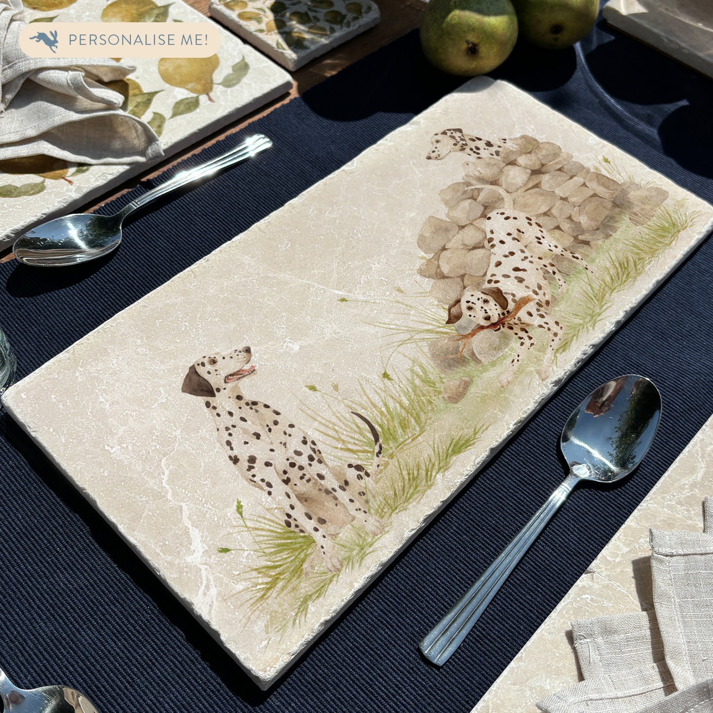 A rectangular marble sharing platter featuring a watercolour design of 3 dalmatian dogs playing fetch in the countryside. The platter is set on a dining table.