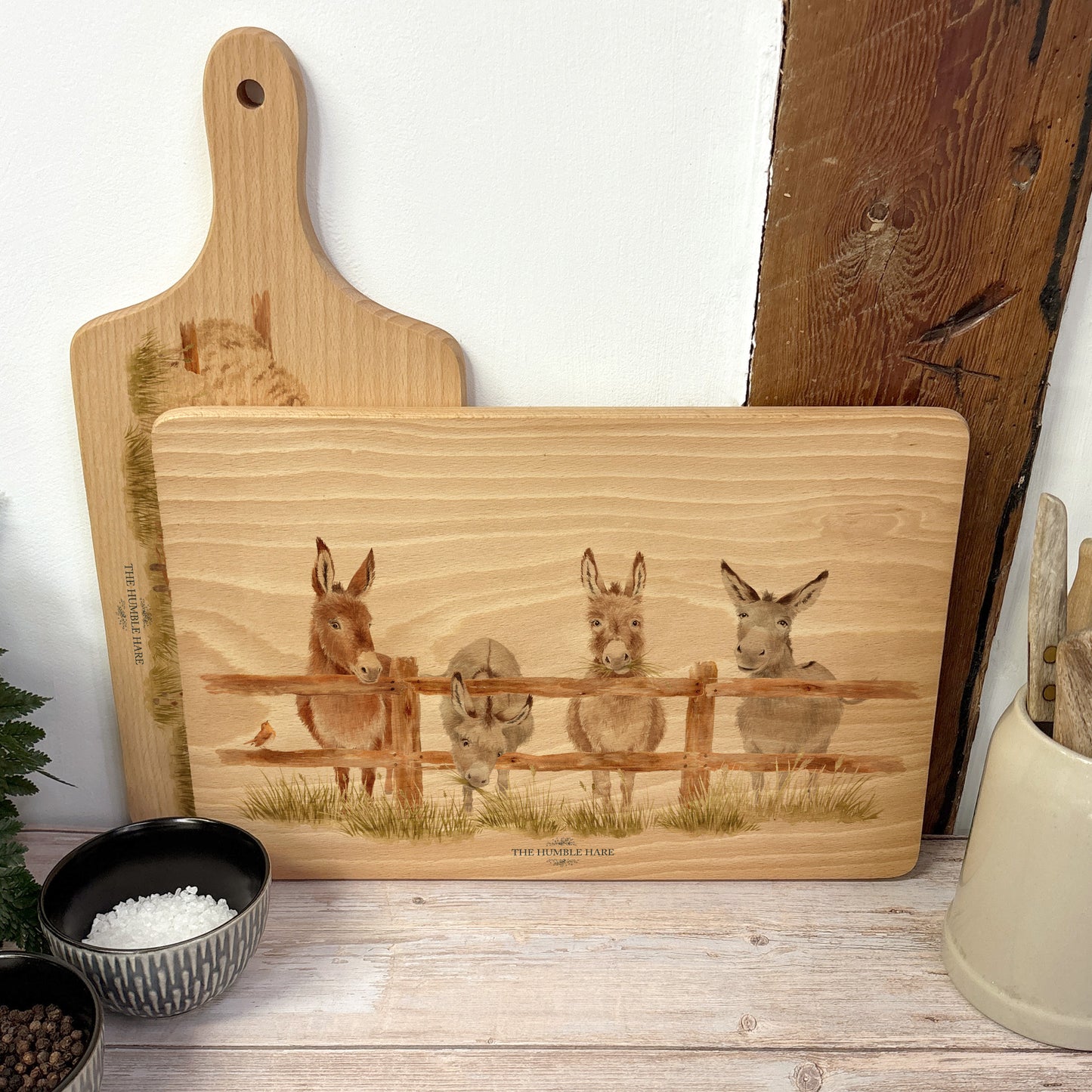 Rectangle wooden chopping board on a kitchen worktop. The beech wood board features  a watercolour design of cheeky donkeys peering over their fence.