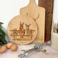 Round wooden chopping board on a kitchen worktop. The beech wood board features a watercolour design of cheeky donkeys peering over their fence.