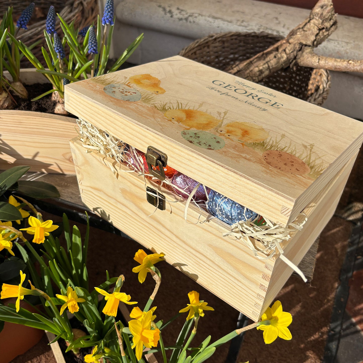 This wooden keepsake box is a large Easter box, perfect for creating a box full of Easter eggs and treats. The box is great for storing keepsakes in once the Easter treats have been eaten. This design has 3 chicks, the three chicks are looking at the pastel colour easter eggs on the floor  wondering if any more chicks may hatch or not. This gift box is full of easter chocolate treats 