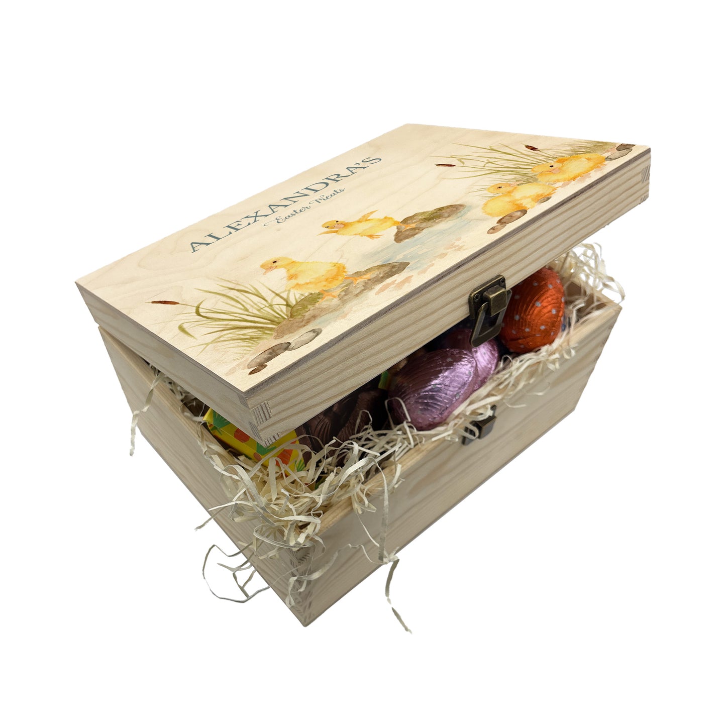 Small Easter personalised wooden pine box, perfect for Easter treats, eggs, gifting. Children gifts. This box has a beautiful easter theme with 4 fluffy ducklings playing in a pond area, surrounded by reeds and pebbles. This box can be personalised in 4 phrases or it can just have the design and no text. This box is showing an example of an easter box full with yummy easter treats, eggs, chocolate and biscuits. Perfect for gifting to parents, children and friends 