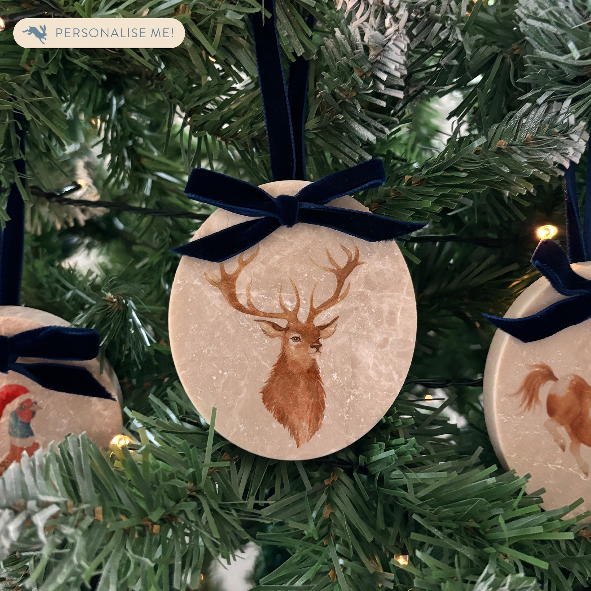 An oval marble bauble featuring a watercolour stag, personalised with your choice of text to create a Christmas decoration unique to you! The bauble is finished with a velvet ribbon.