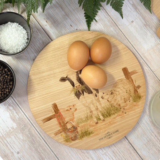 Round wooden chopping board on a kitchen worktop. The beech wood board features a watercolour design full of farm animals, including the dairy cow, grazing horse, sheep, piglets, ducklings and chicken.