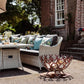 A handmade horseshoe fire pit next to a seating area in the garden of a country house. The fire pit has been filled with firewood and has an authentic rust finish.