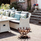 A handmade horseshoe fire pit next to a seating area in the garden of a country house. The fire pit has been filled with firewood and has an authentic rust finish.