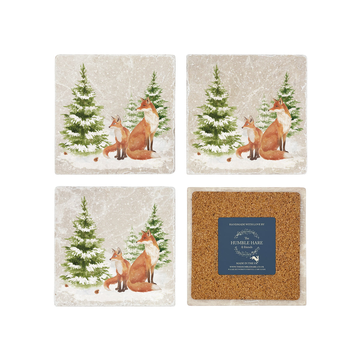 Set of four square marble coasters featuring a winter forest illustration with a fox family and evergreen trees in the snow. One coaster is flipped to show the back is covered with cork to protect surfaces.