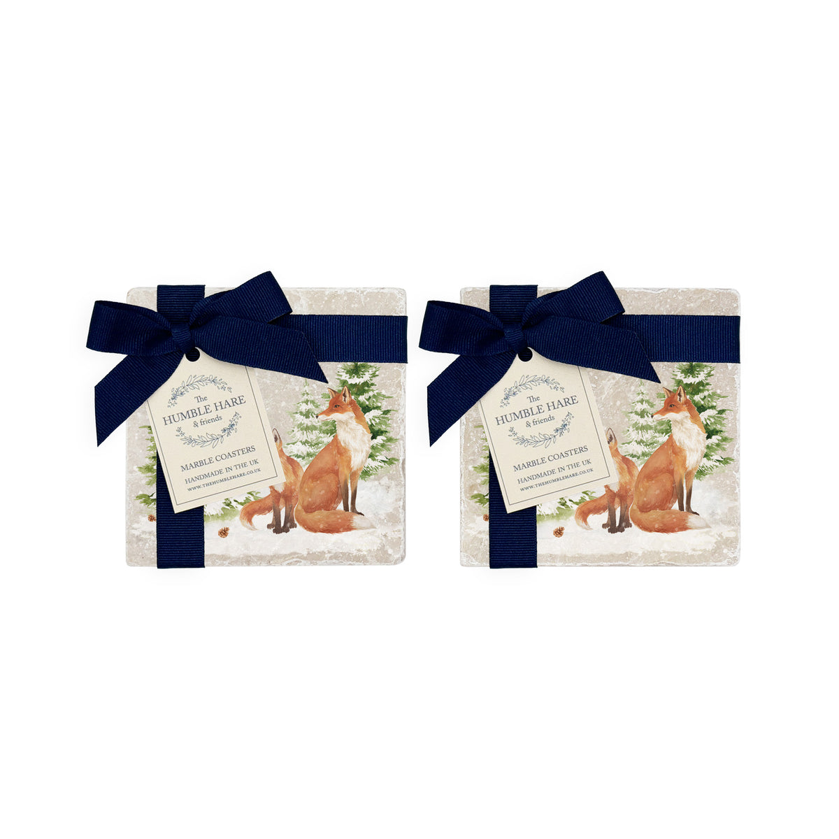 Set of four square marble coasters featuring a winter forest illustration with a fox family and evergreen trees in the snow. The coasters are bowed in two pairs with a navy blue ribbon.