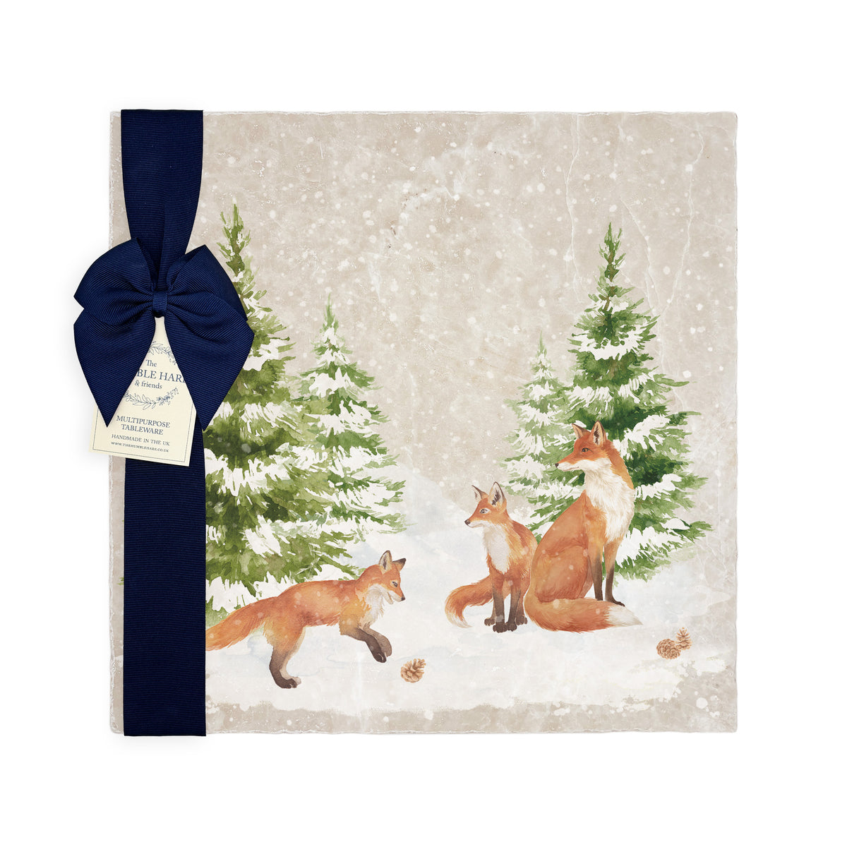 A large square marble platter featuring a forest scene with a fox family playing in the snow. The platter is wrapped with a dark blue gift ribbon and paper tag.