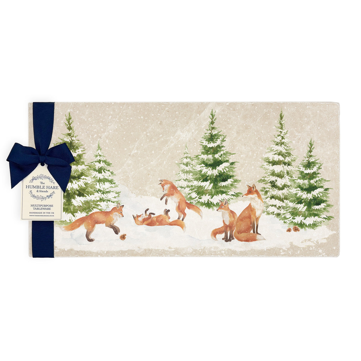A rectangular marble sharing platter with a winter scene of a family of foxes and fox cubs playing in the snow. The platter is packaged with a navy blue bow and paper gift tag.