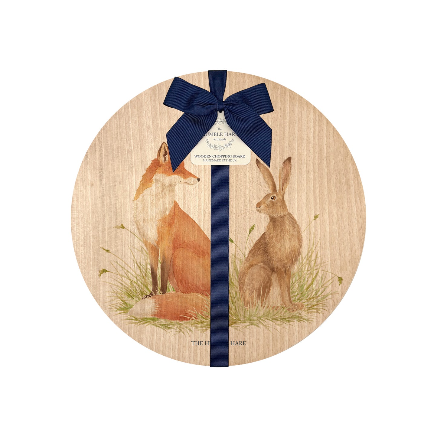 Round beech wood chopping board featuring a watercolour design of a fox and hare in a meadow. The wooden board is finished with a blue gift ribbon and tag.