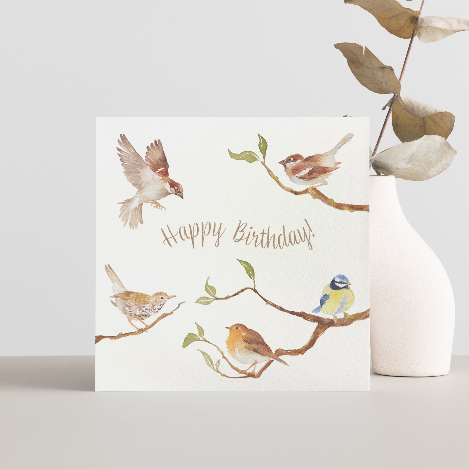 A greetings card reading Happy Birthday in brown text surrounded by garden birds on branches in a watercolour style.