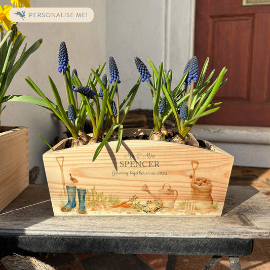 An arched wooden planter box with a gardening scene watercolour design, including welly boots, watering can, sack of potatoes, garden fork and spade, plus a little robin. The planter can be personalised with a name and a selection of custom phrases. Perfect gift for gardeners and special occasions.