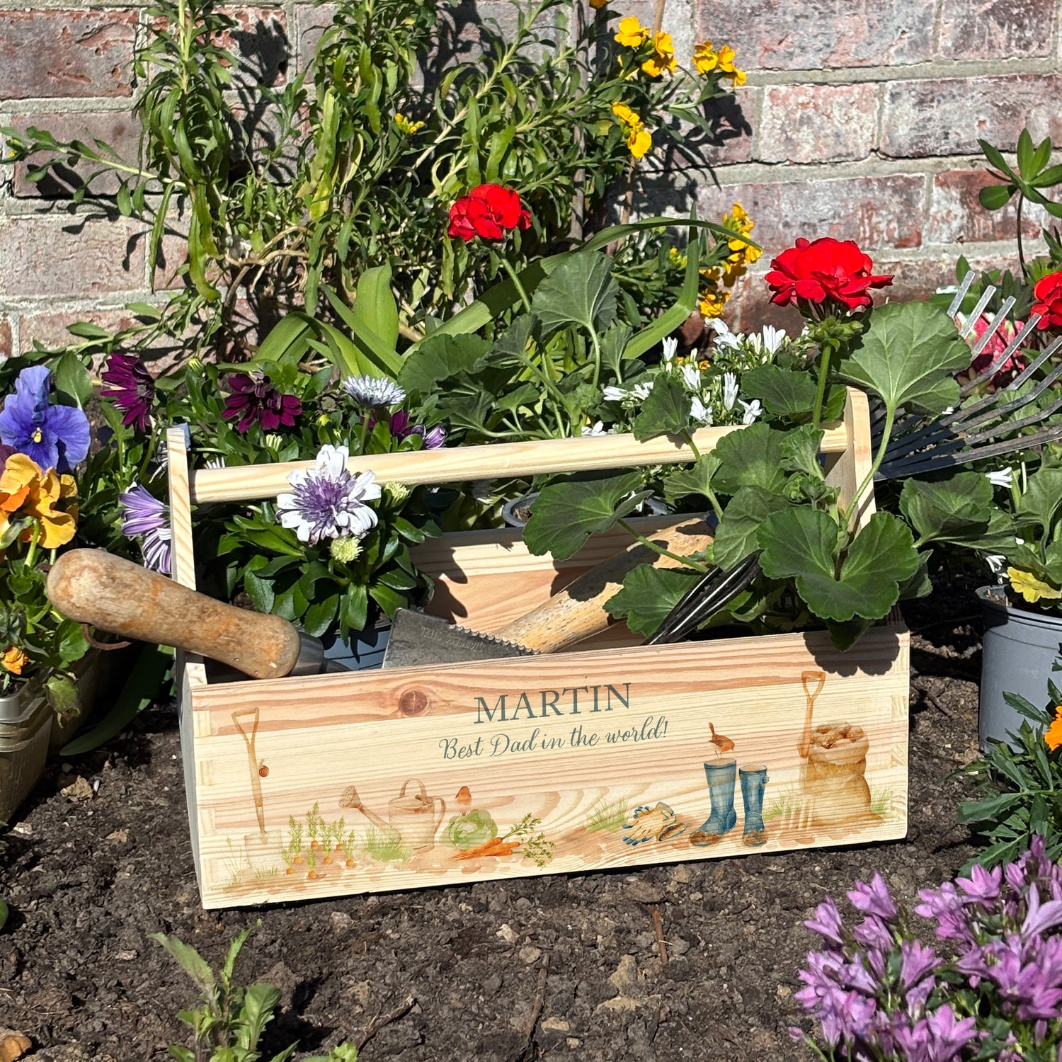 wooden luxury Trug/Caddy the perfect personalised gift. Each product is lovingly designed, handmade with our Countryside inspired watercolour designs. This design features a gardening scene with wellie boots, a sake of potatoes, vegetables, a watering con and a little robin. set in a flower bed unique designs for a truly one off special occasion for a loved one. 