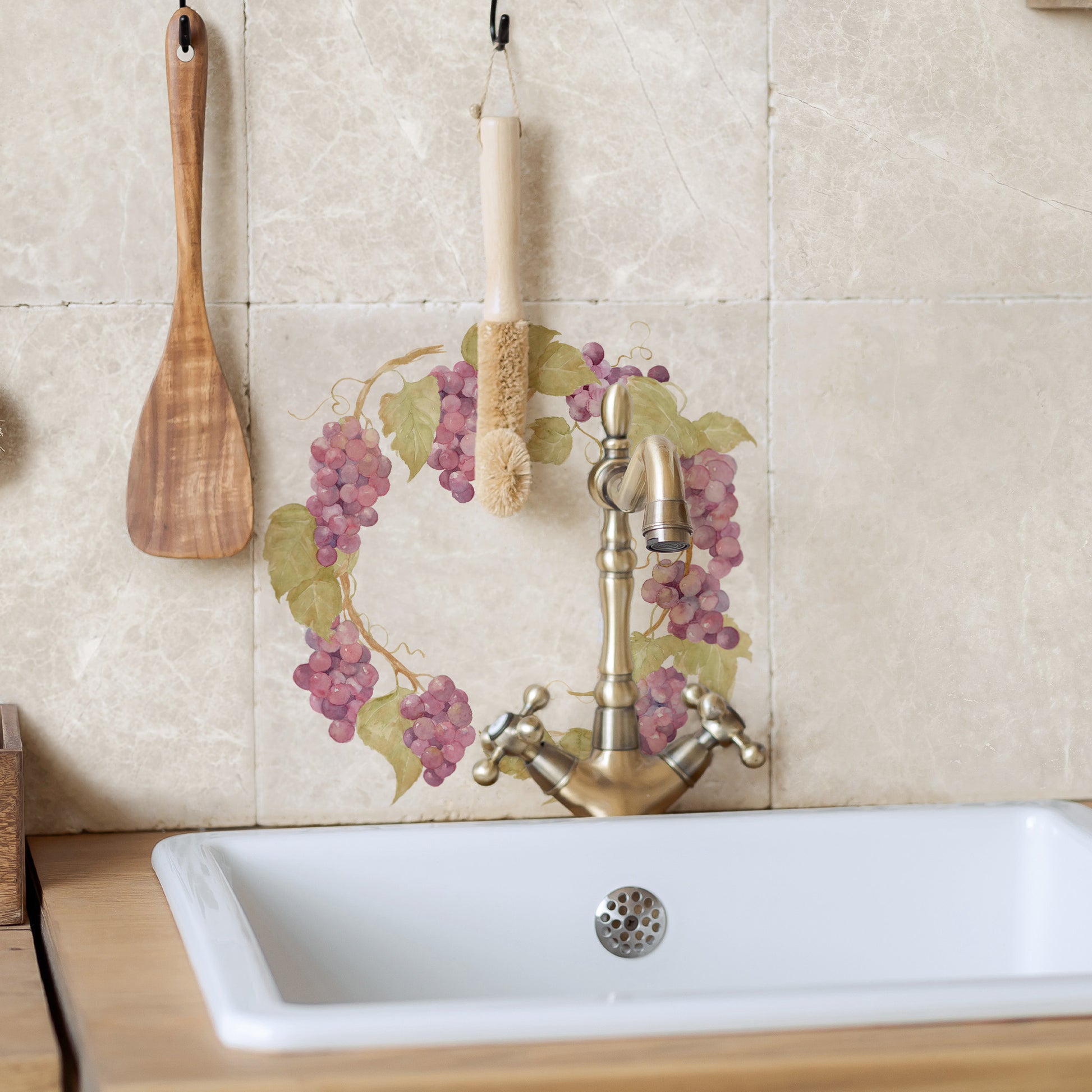 A large square marble splashback tile set behind a country kitchen sink. The tile has a grape wreath design.