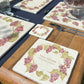A medium square marble personalised platter featuring a watercolour grape vine wreath design. The platter is set on a dinner table next to a marble placemat and coaster.