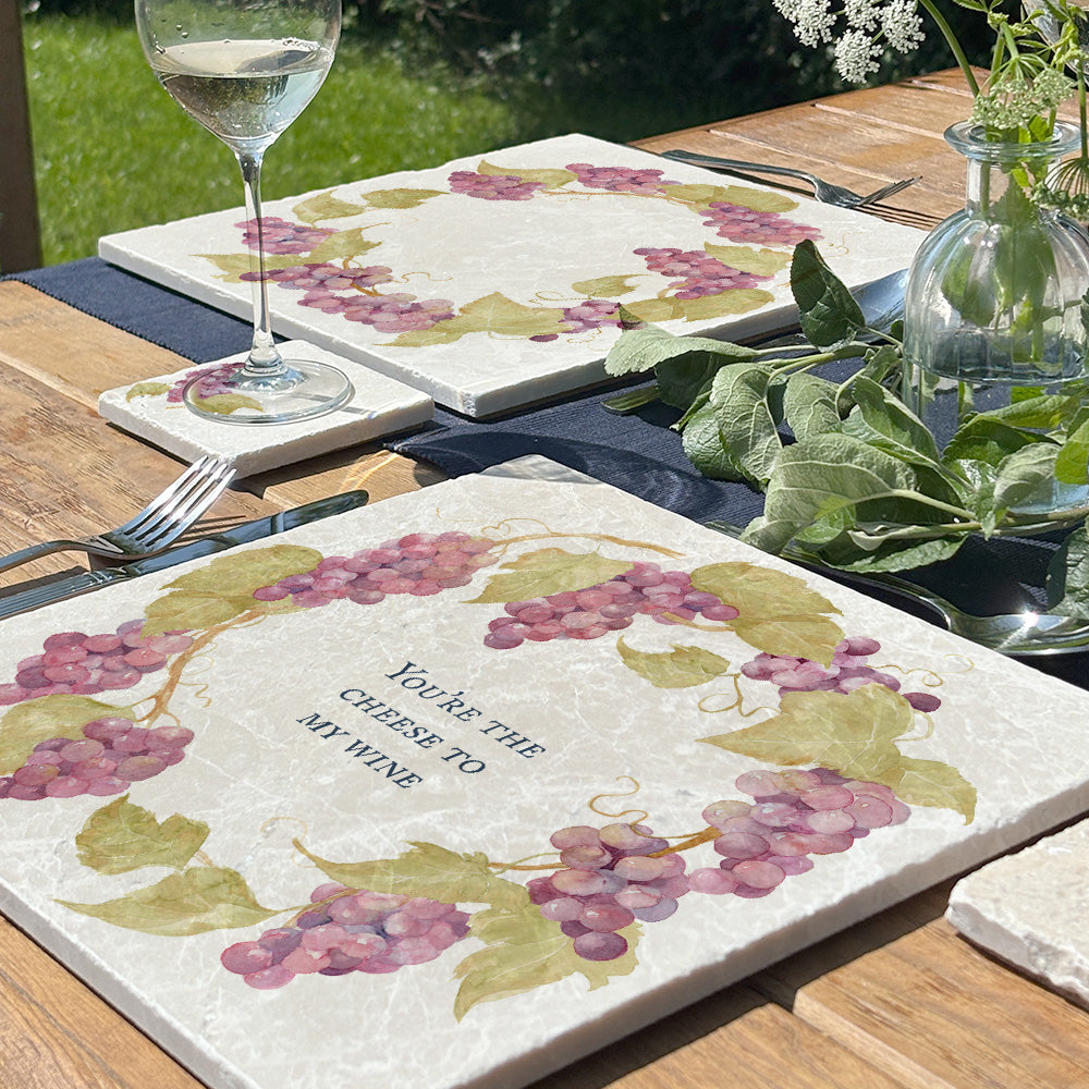 A large marble placemat personalised with the bespoke message ‘You’re the cheese to my wine’. The placemat is set on a table in a sunny garden.