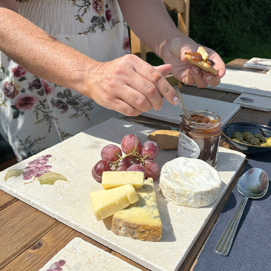 An elegant outdoor dining table set with a marble cheeseboard featuring a minimalistic grape vine design.