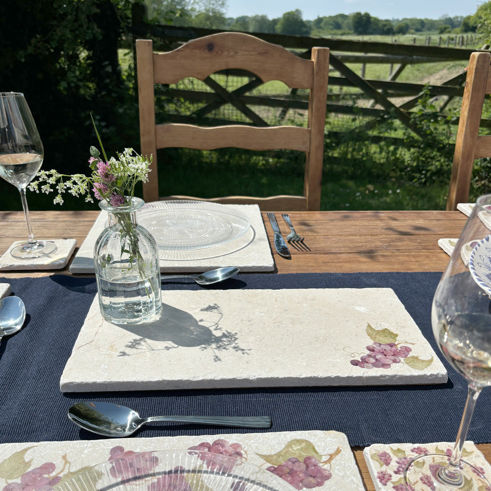 A garden table set with marble placemats and serving platters featuring a minimalistic grape vine watercolour design.