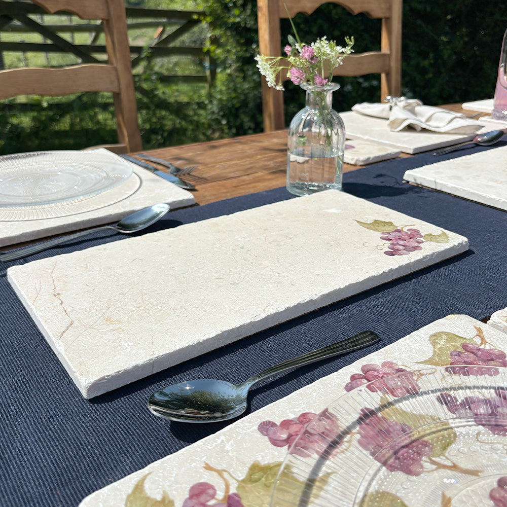 A rectangular cream marble sharing board with a minimalistic bunch of grapes design. The platter is set on an al fresco dining table in the summer sunshine.