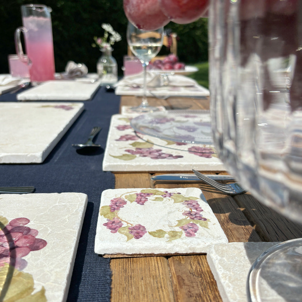 An al fresco dining table set with marble coasters and placemats featuring a watercolour grape vine wreath design.