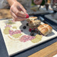 A large marble platter featuring a watercolour grape vine wreath design. The platter is being used as a serving board for fruit and desserts.