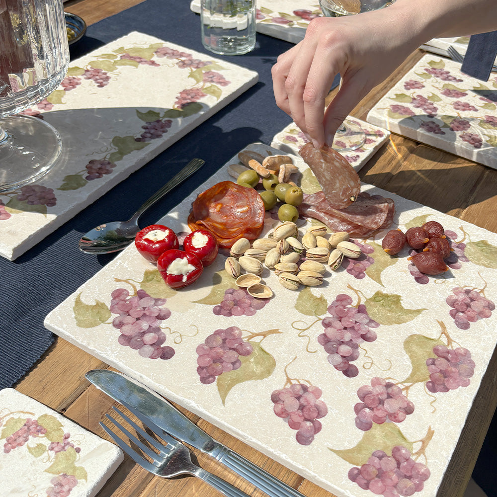 A dinner table in the sunshine set with marble tableware, including a handmade marble sharing platter featuring a grape vine wreath design.