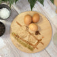 Round wooden chopping board on a kitchen worktop. The beech wood board features a watercolour design of mischievous sheep escaping their field.