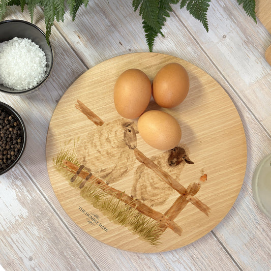 Round wooden chopping board on a kitchen worktop. The beech wood board features a watercolour design of mischievous sheep escaping their field.