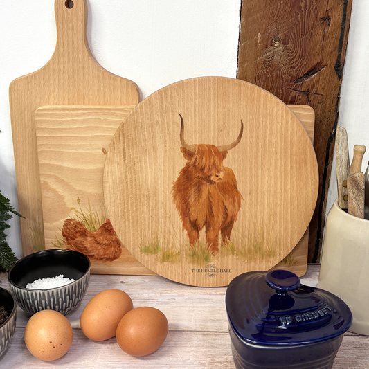 Handmade wooden chopping board featuring a watercolour Highland cow illustration, tied with blue ribbon.