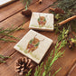 Set of four square marble coasters featuring a watercolour illustration of a Highland cow wearing a green wreath with red tartan bow.