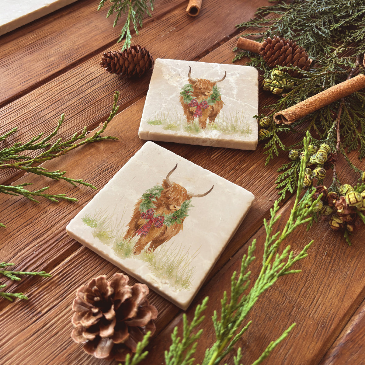 Set of four square marble coasters featuring a watercolour illustration of a Highland cow wearing a green wreath with red tartan bow.