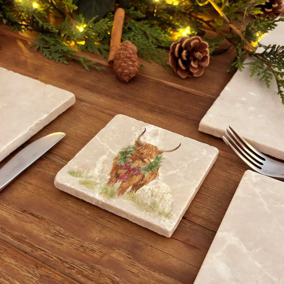Set of four square marble coasters featuring a watercolour illustration of a Highland cow wearing a green wreath with red tartan bow.