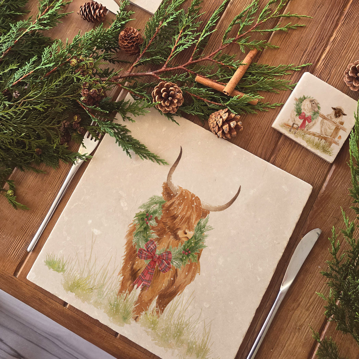 A large square marble placemat with a watercolour highland cow wearing a Christmas wreath around his neck.