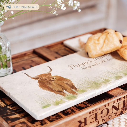 A marble sharing platter featuring a highland cow, personalised with neutral colour text. The marble platter is set on a breakfast tray and is being used to serve pastries.