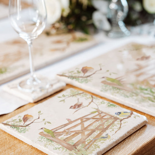 A wooden dining table set with a medium marble platter, with a watercolour design featuring British garden birds in the hedgerow around the paddock gate.
