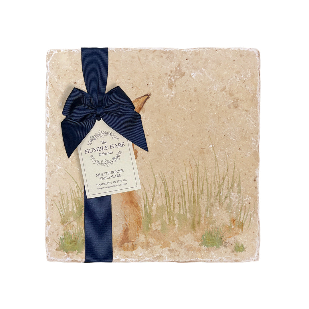 A multipurpose marble platter with a watercolour design featuring a hare washing his ear, packaged with a luxurious dark blue bow and branded gift tag.